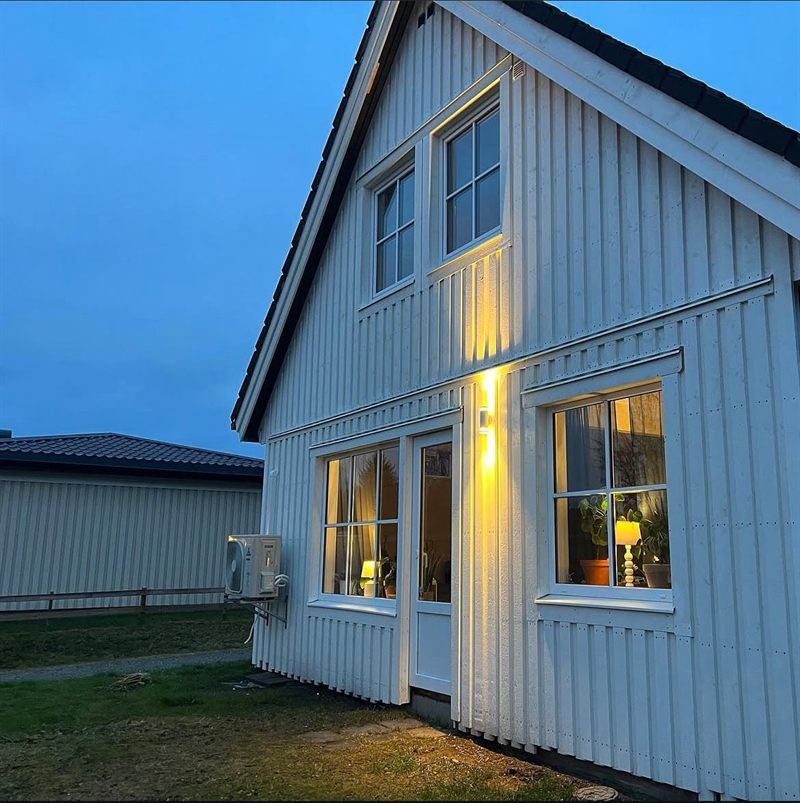 Hus med nybytt vitt fasadpanel i skymningsljus, med fönster och veranda