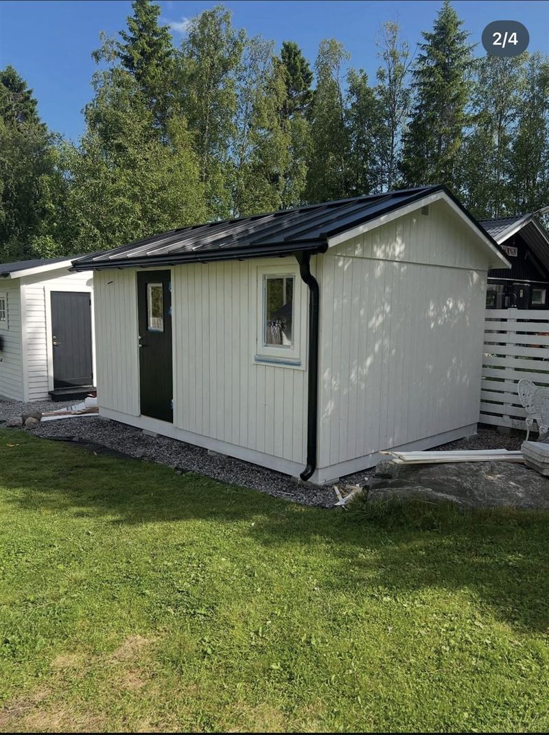 Nybyggd friggebod på 15 kvm med vit panel, svart plåttak och grön dörr