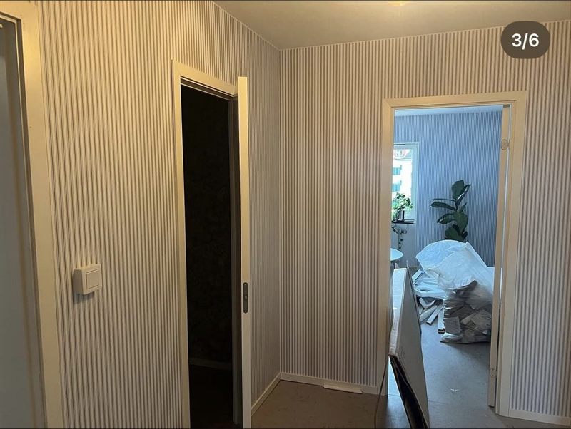 Nyrenoverad hall med randig tapet, vita dörrfoder och golvlister
